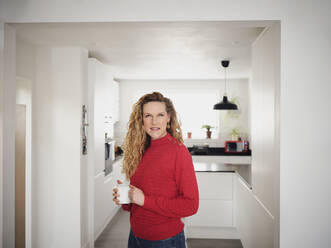 Lächelnde Frau mit Kaffeetasse in der Hand in der Küche stehend - PWF00347