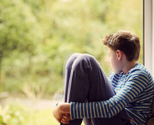 Boy looking through window at home - PWF00357