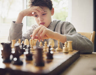 Junge mit Kopf in der Hand spielt Schach zu Hause - PWF00361