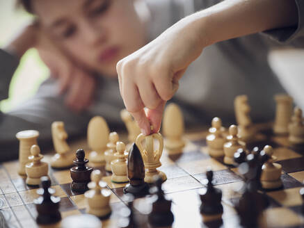 Boy holding chess piece while playing at home - PWF00363