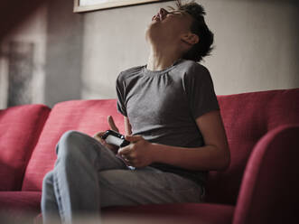 Enttäuschter Junge mit Gamecontroller auf dem Sofa zu Hause - PWF00366
