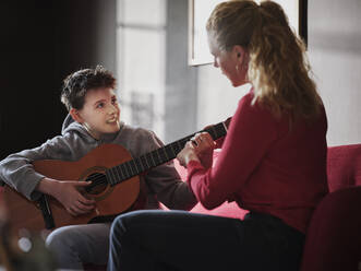 Mother assisting son plying guitar at home - PWF00367