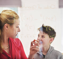 Mother looking at smiling son while teaching mathematics on glass - PWF00371