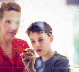 Junge schreibt mit seiner Mutter auf Glas, während er zu Hause Mathematik lernt - PWF00372