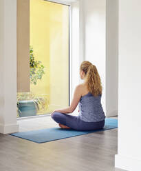 Blonde Frau meditiert zu Hause vor dem Fenster - PWF00378