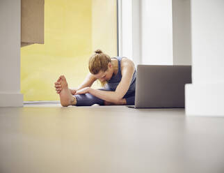 Mature woman doing stretching exercise in front of laptop at home - PWF00380