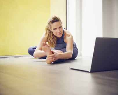 Mature woman practicing exercise while using laptop at home - PWF00381