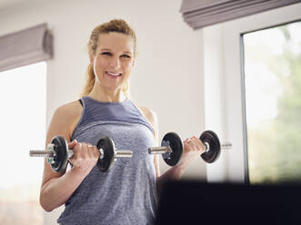 Smiling woman holding weights while exercising at home - PWF00392