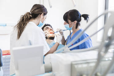 Zahnärztin mit Assistentin beim Bohren der Zähne eines männlichen Patienten in einer Klinik - WPEF04467