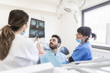 Zahnärztin mit Assistentin, die einem Patienten in einer medizinischen Klinik eine Röntgenaufnahme erklärt - WPEF04474