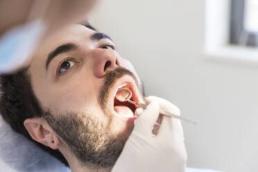 Female dentist with angled mirror examining male patient's teeth at medical clinic - WPEF04475