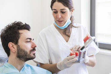 Eine Zahnärztin erklärt einem Patienten in einer medizinischen Klinik ein Zahnmodell - WPEF04477