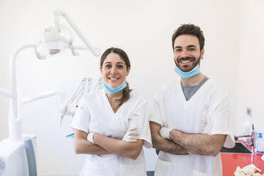 Smiling female and male dentists standing with arms crossed in medical clinic - WPEF04484