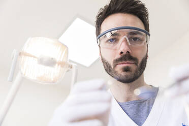 Männlicher Zahnarzt mit Schutzbrille bei der Arbeit in einer medizinischen Klinik - WPEF04485