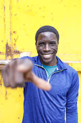 Smiling man pointing while standing in front of yellow wall - IFRF00631