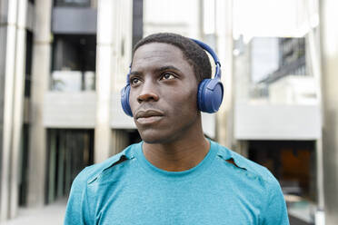 Afro-Mann, der nachdenklich ist, während er über Kopfhörer am Gebäudeeingang Musik hört - IFRF00636