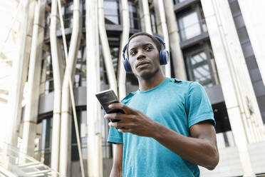Mann mit kabellosen Kopfhörern und Mobiltelefon vor einem Gebäude - IFRF00637