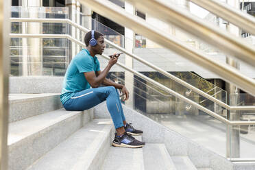 Man wearing headphones sending voicemail while sitting on staircase - IFRF00638