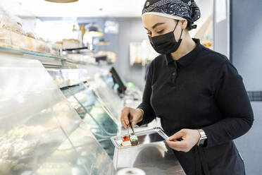 Weibliche Besitzerin mit Kuchen auf einem Tablett in der Vitrine einer Bäckerei - IFRF00676