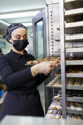 Unternehmerin, die in einer Bäckerei ein Tablett ins Regal stellt - IFRF00688