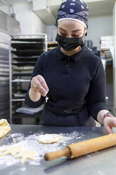 Bäckerin bestreut Mehl beim Ausrollen von Teig in einer Bäckerei - IFRF00699