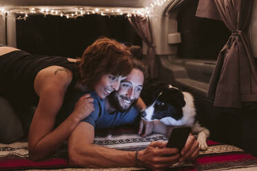Glückliches Ehepaar mit Smartphone und Hund im Van - EBBF03535
