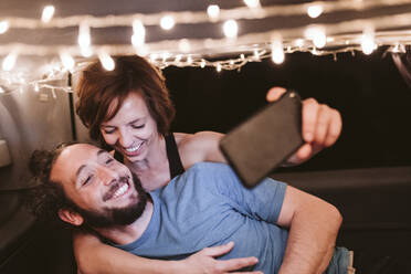 Lächelndes Paar macht Selfie in beleuchtetem Van bei Nacht - EBBF03536