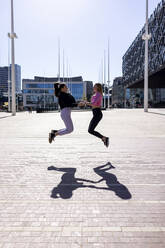 Female friends jumping on footpath during sunny day - WPEF04509