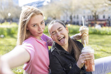 Junge Frau, die bei einem Milchshake im Park ein Gesicht von ihrer Freundin macht - WPEF04513