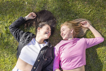 Happy women lying on grass at public park - WPEF04523