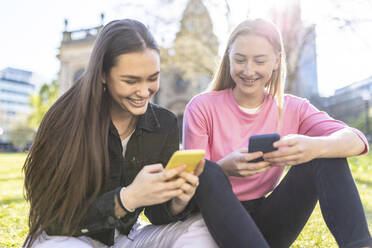 Lächelnde Frauen benutzen ihr Smartphone im Park - WPEF04531