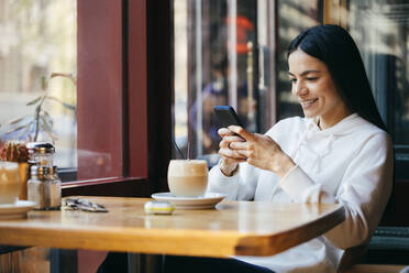 Smiling woman using mobile phone at cafe - OYF00352