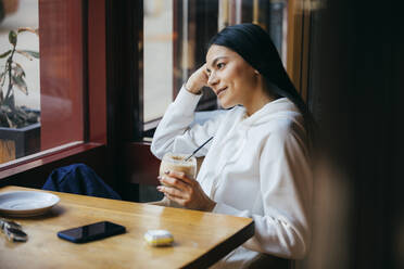 Smiling woman looking away while holding drink at cafe - OYF00355