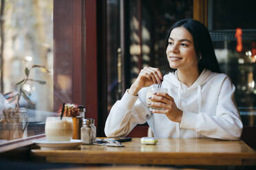 Nachdenkliche Frau mit Strohhalm beim Kaffeetrinken im Café - OYF00359