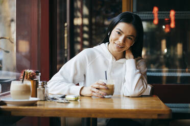 Smiling woman with coffee sitting at cafe - OYF00361