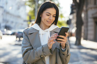 Smiling woman using smart phone in city - OYF00367