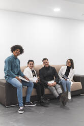 Fröhliche männliche und weibliche Fachkräfte sitzen auf dem Sofa im Büro - JAQF00651