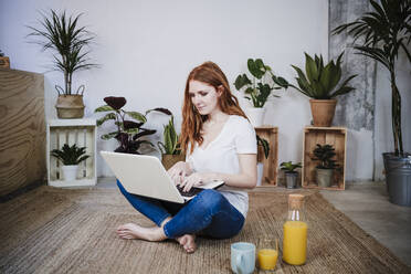 Young redhead woman using laptop while sitting on floor at home - EBBF03558