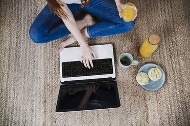 Woman using laptop while having juice at home - EBBF03567