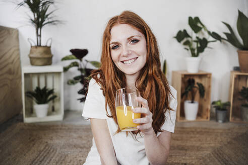 Lächelnde schöne Frau hält ein Glas Saft zu Hause - EBBF03568