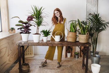 Smiling woman standing in front of potted plants on table at home - EBBF03574