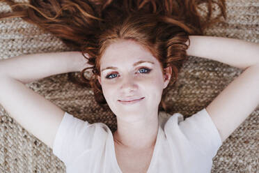 Smiling beautiful woman lying on floor at home - EBBF03589