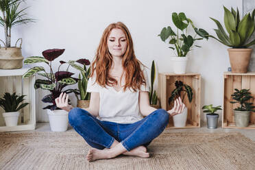 Redhead woman meditating while sitting on floor at home - EBBF03591
