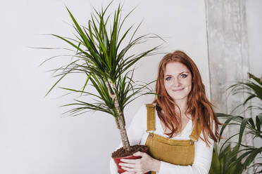 Schöne junge Frau hält Zimmerpflanze zu Hause - EBBF03606