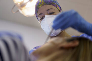 Female dentist wearing protective face mask examining patient's teeth at clinic - JSMF02212