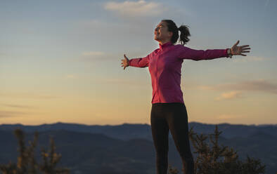 Happy young woman with arms outstretched during sunrise - SNF01425