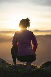 Weibliche Läuferin hockt beim Betrachten des Sonnenaufgangs - SNF01431