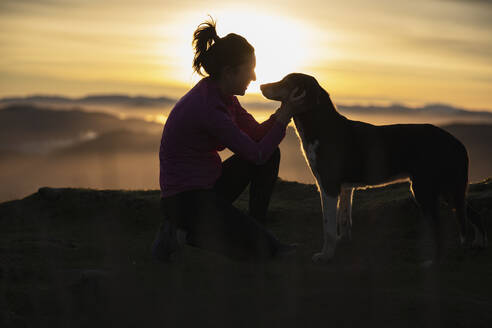 Smiling woman stroking dog while kneeling outdoors - SNF01434