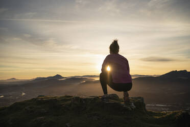 Young woman looking at sunrise while crouching at cliff - SNF01435