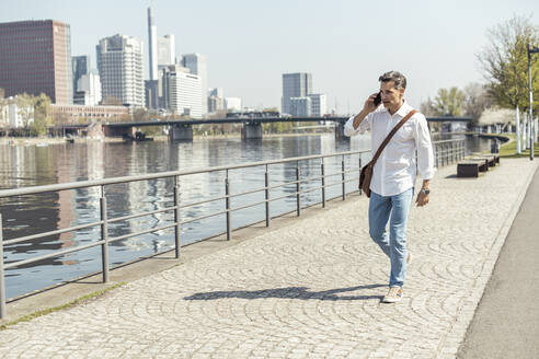 Male entrepreneur talking on mobile phone while walking in city - UUF23160